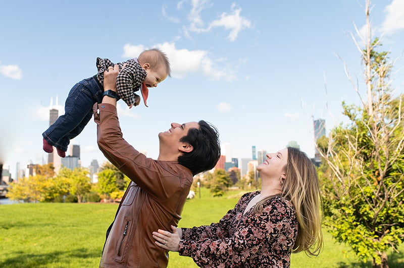 Parents and their infant in a park with a view of the city behind them